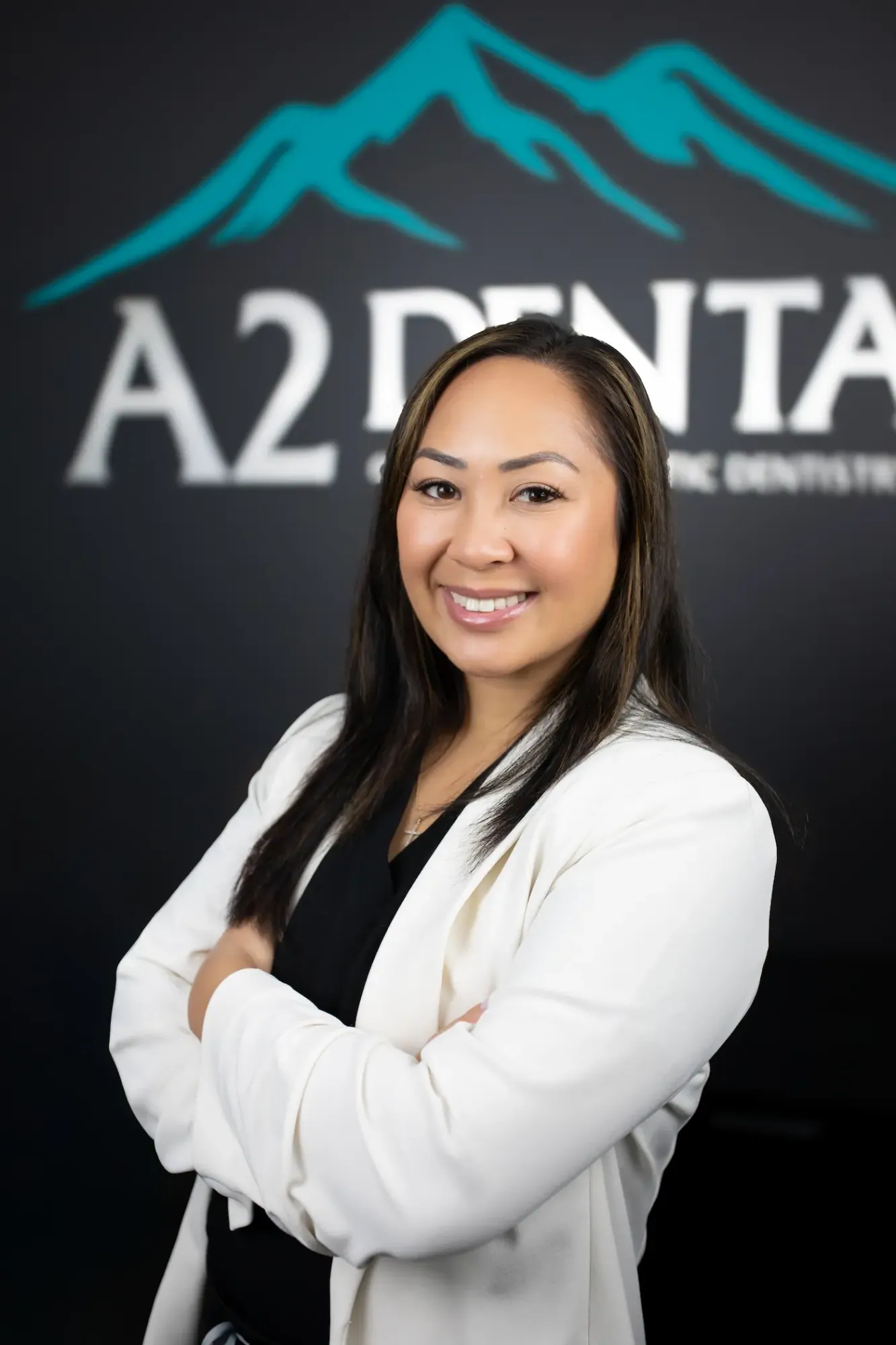 Dr. Kim Bernales, DDS, smiling in front of the A2 Dental logo wall
